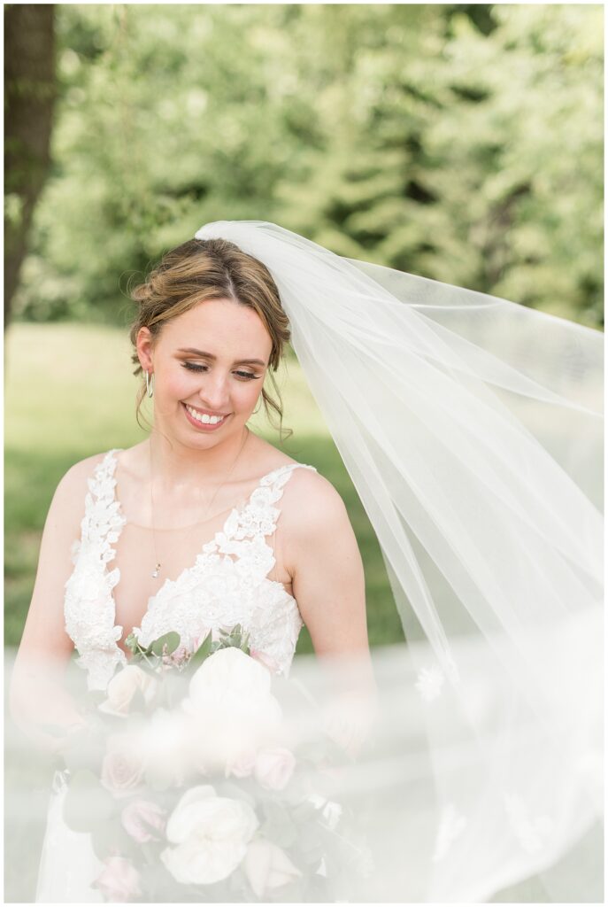 bride looking down and smiling with her long veil blowing around her on sunny day at the barn at silverstone