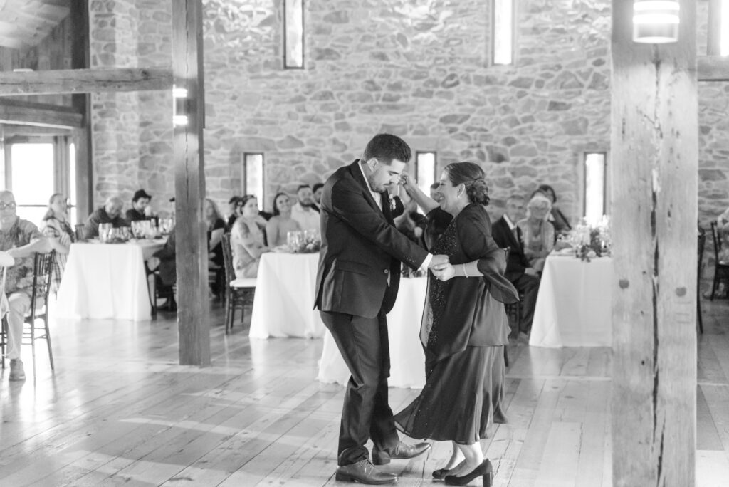 black and white photo of groom and his mom dancing with guests watching at the barn at silverstone
