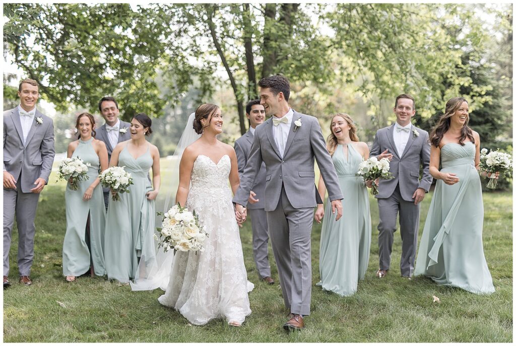 couple holding hands and walking towards camera as they smile and their bridal party follows them in wrightsville pennsylvania