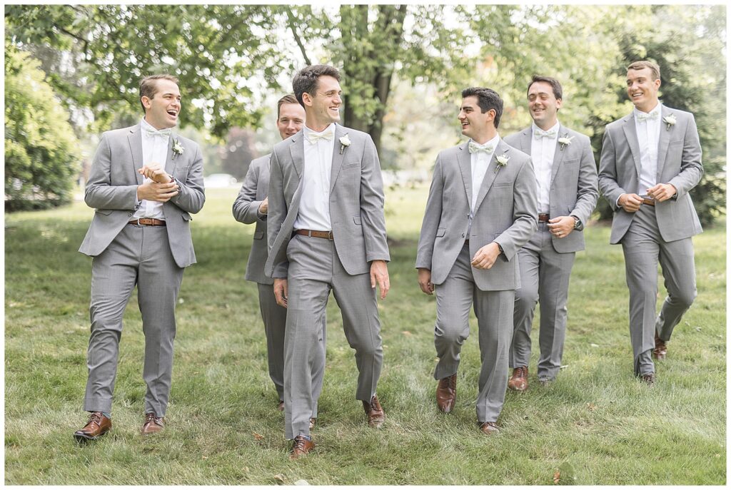 groom with his five groomsmen all in dark gray suits with white bowties walking outdoors at historic ashland
