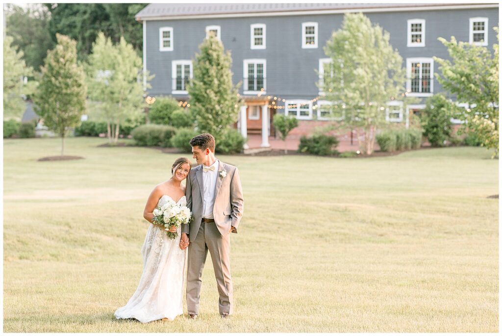 bride rests her left cheek against groom's right shoulder as he looks down at her by gray barn at historic ashland
