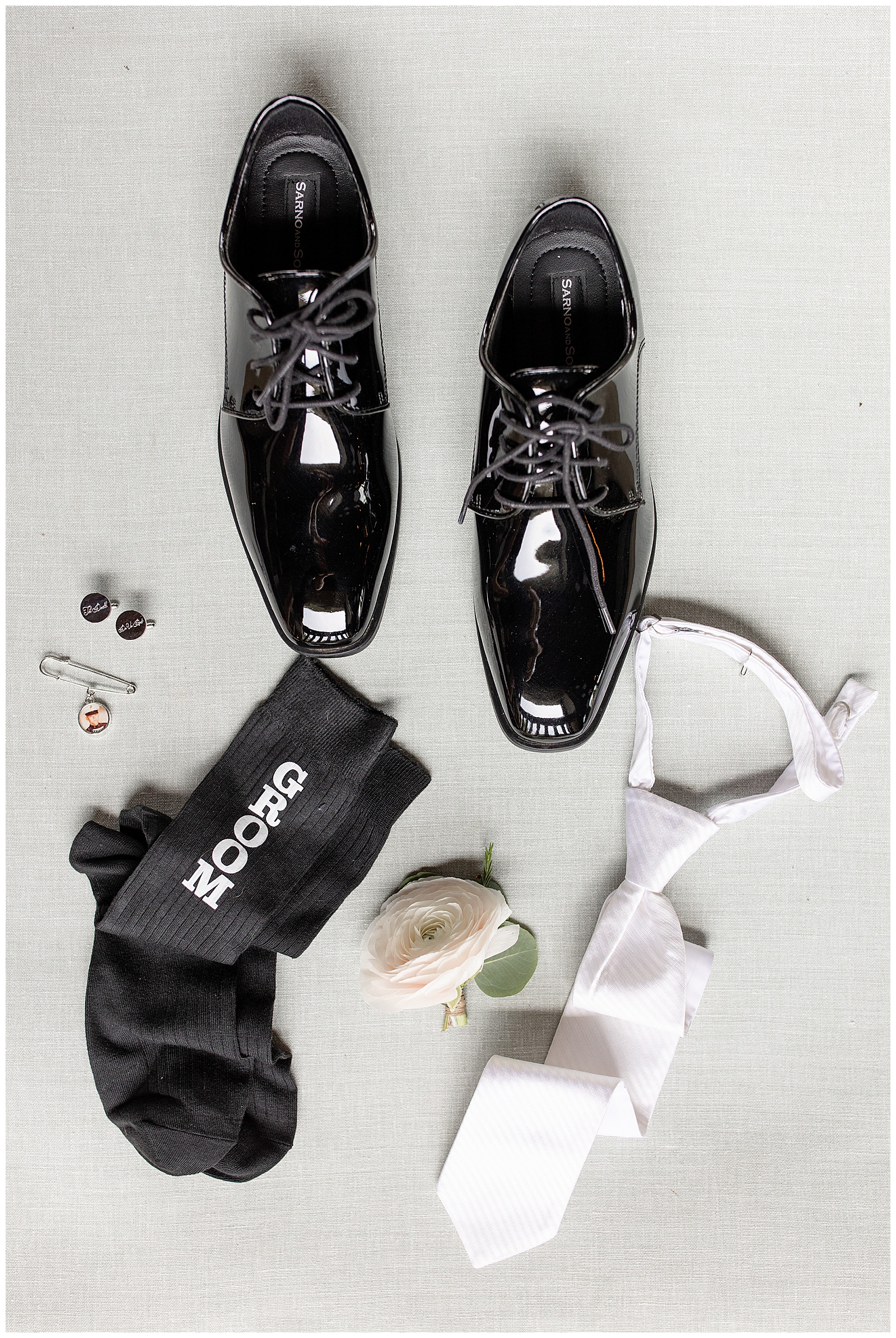 groom's shiny back shoes, white tie, and accessories displayed on white background at stoltzfus homestead