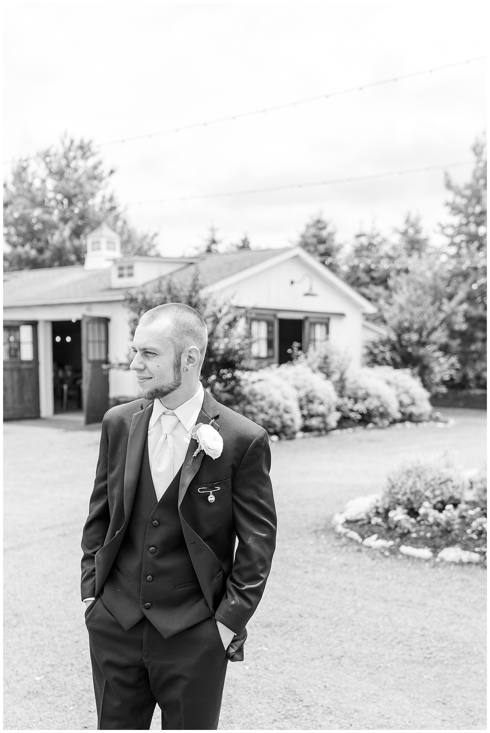 black and white photo of groom in black suit with black vest and hands in his pockets looking to his right with building behind him in lancaster pennsylvania