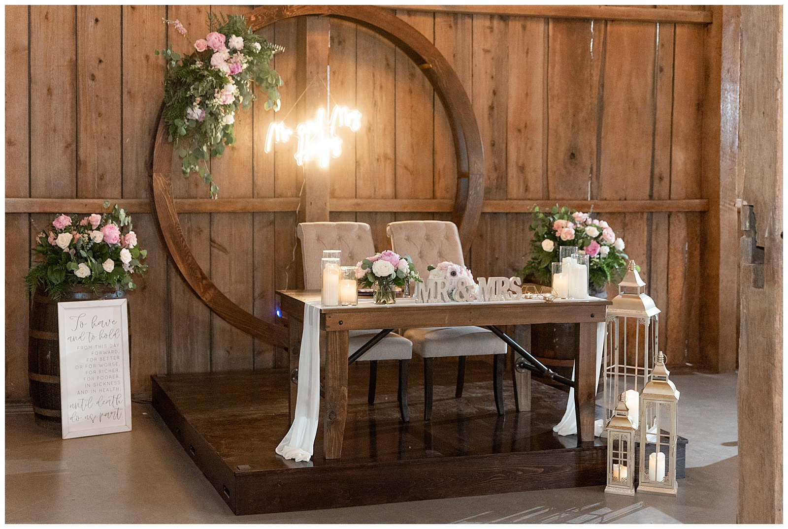 wooden couples table with round wooden structure behind them beautifully decorated inside barn at venue in gordonville pennsylvania