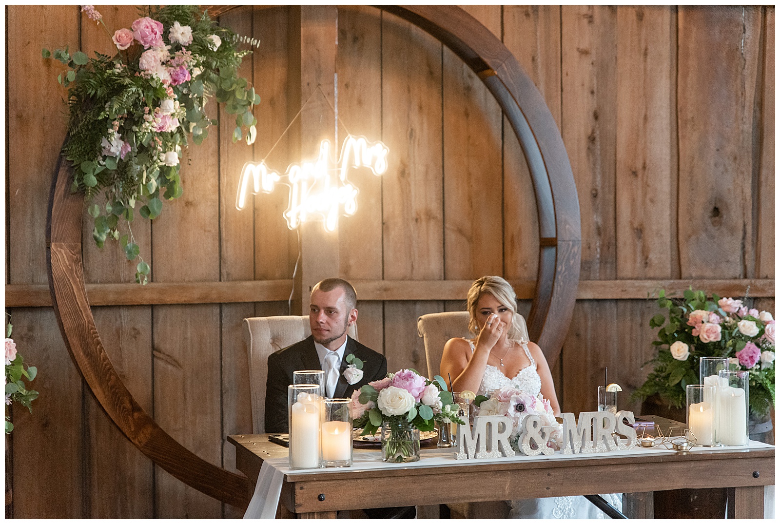 bride and groom sitting at their couples table as bride wipes her eye with tissue during reception at lancaster county barn venue