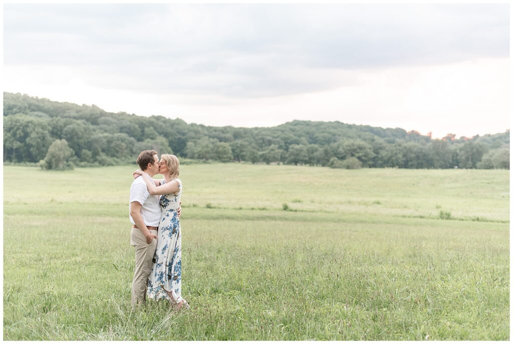 couple standing in large open field kissing on overcast evening at valley forge national park in pennsylvania