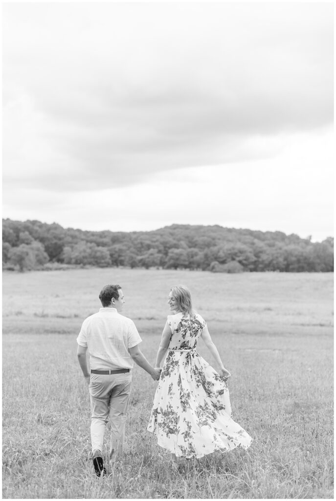 black and white photo of couple walking away from camera in large open field at valley forge national park
