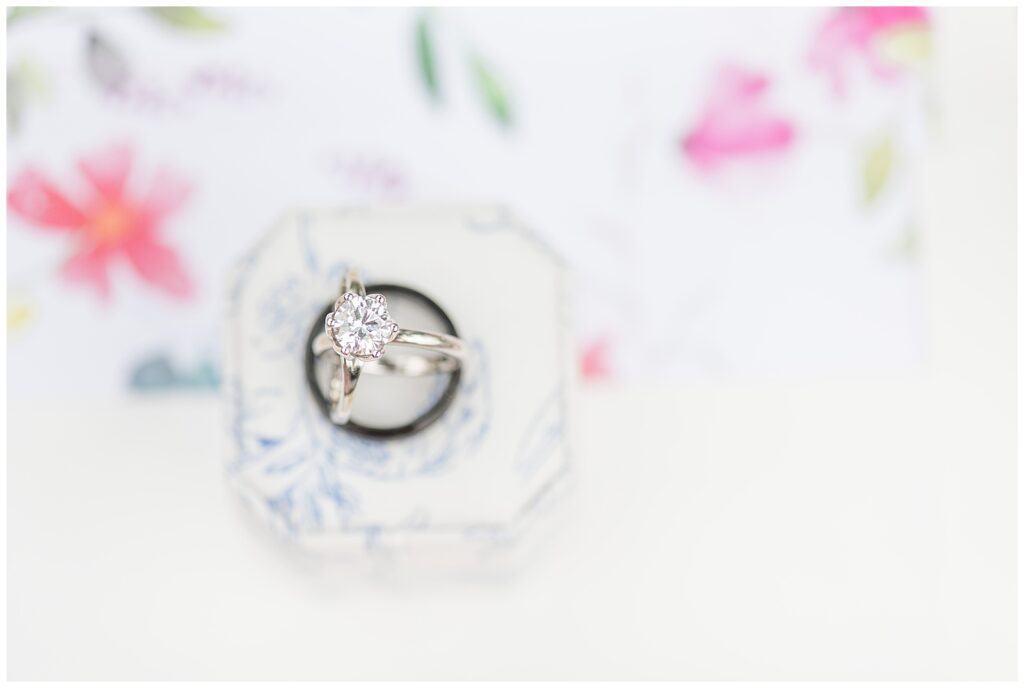 bride's diamond rings sitting inside groom's wedding band atop ring box and wedding invitation in glen mills