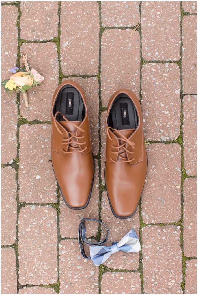 groom's brown dress shoes surrounded by boutonniere, watch, and bowtie on brick path in glen mills pa
