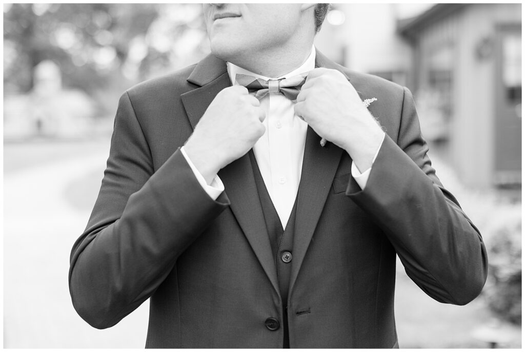 close up black and white photo of groom holding edges of his bowtie at the inn at grace winery