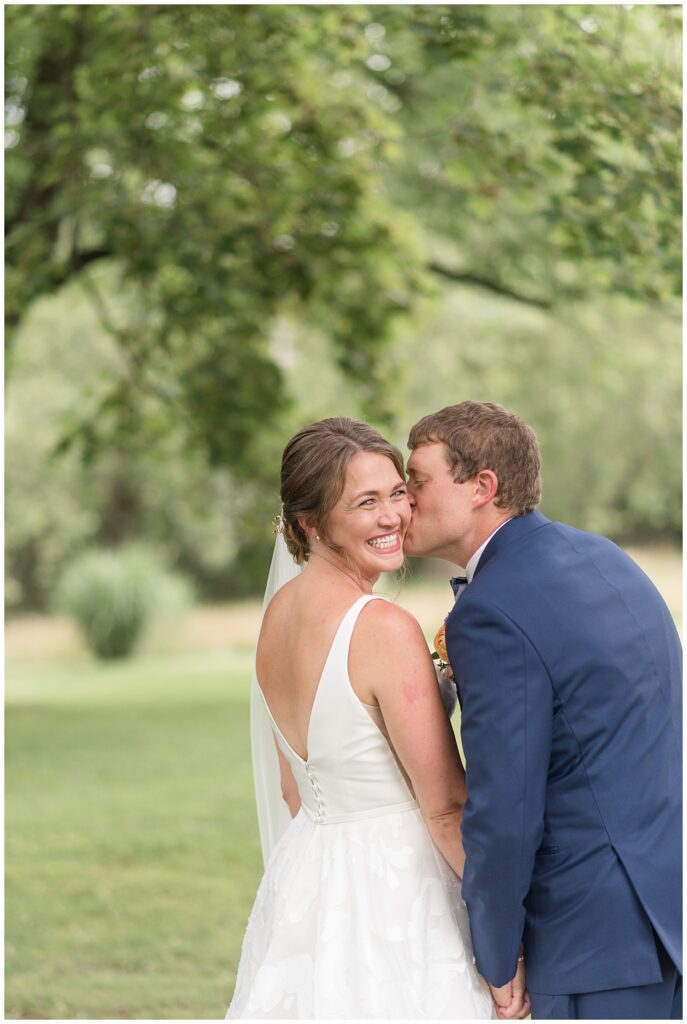 bride looking back and smiling as groom kisses her left cheek with his back towards camera in glen mills