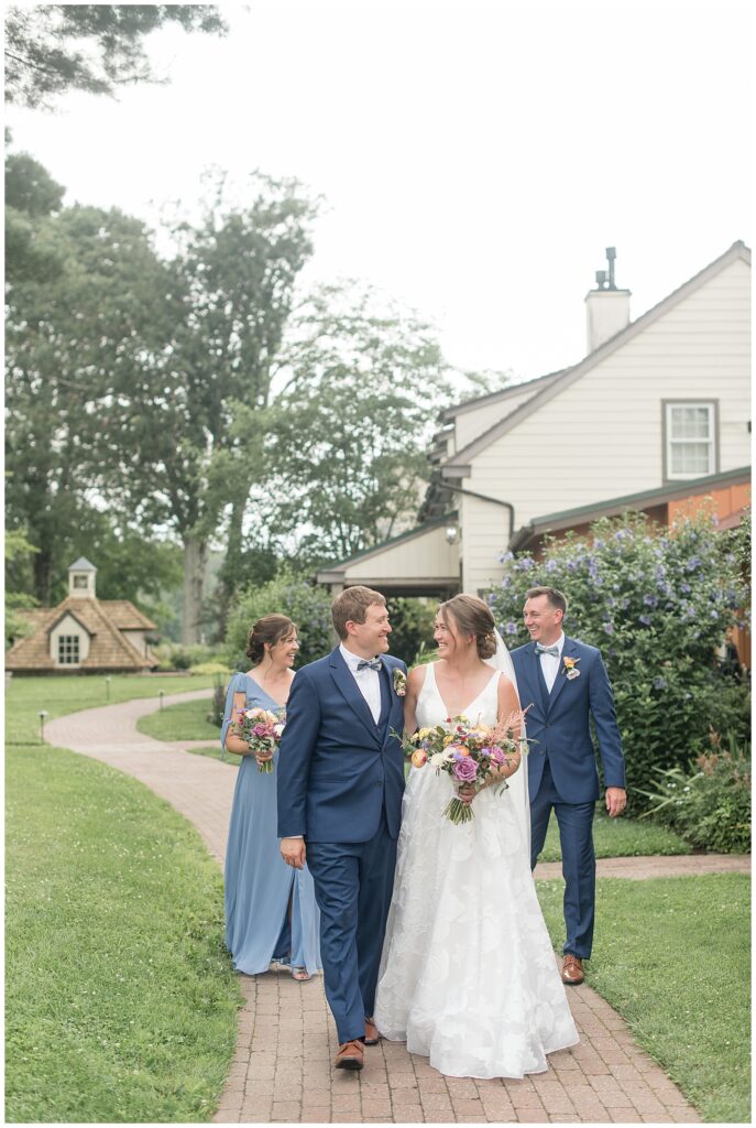 couple smiling and looking at each other with their maid of honor and best man on pathway at the inn at grace winery