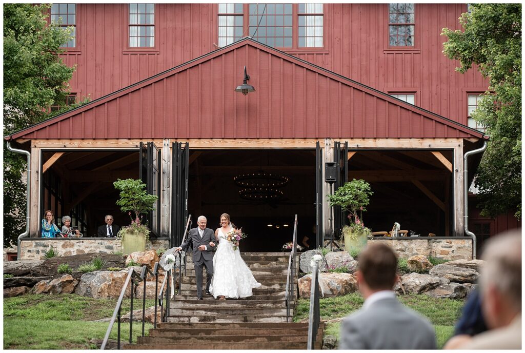 bride and her father walking down the steps of red barn towards the guests watching at the outdoor wedding in glen mills pennsylvania