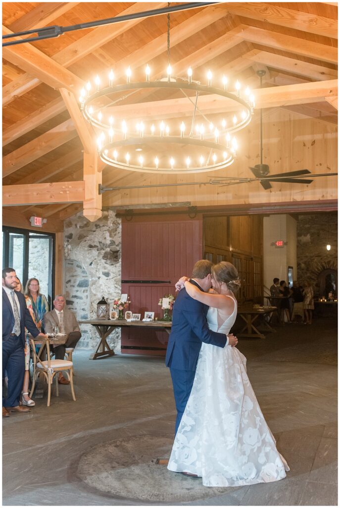 bride and groom sharing their first day under chandelier inside barn at the inn at grace winery in pennsylvania