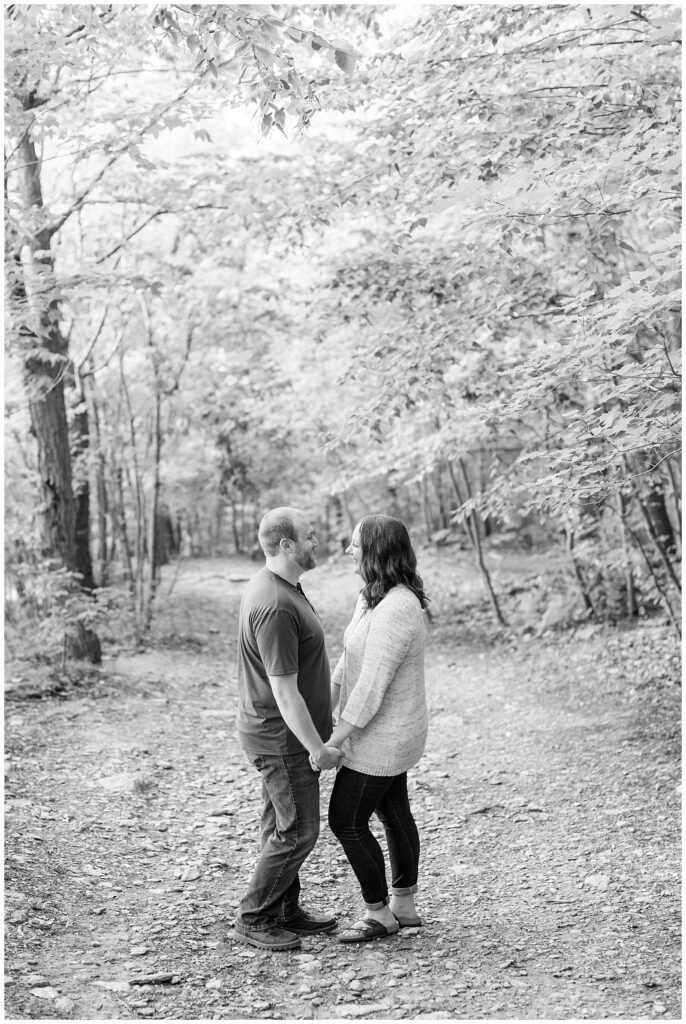 black and white photo of couple facing each other holding hands on path surrounded by trees at pinnacle point
