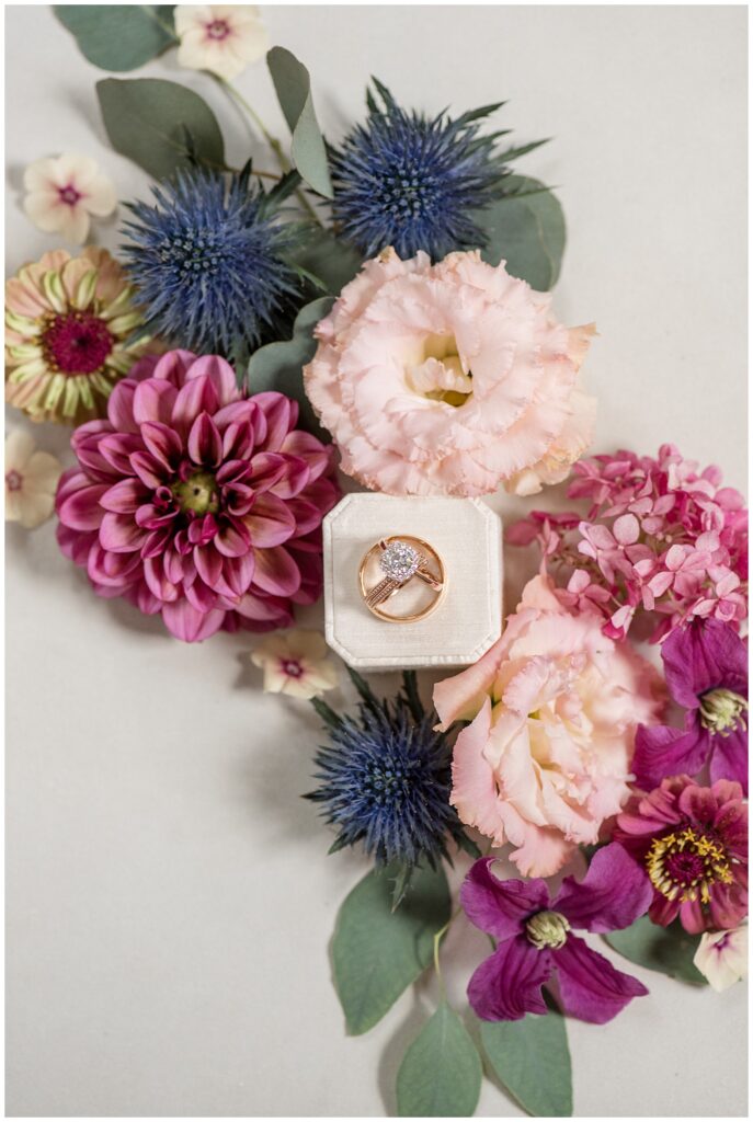 wedding rings setting in ivory velvet box surrounded by maroon, light pink, and navy blue flowers in lancaster pa