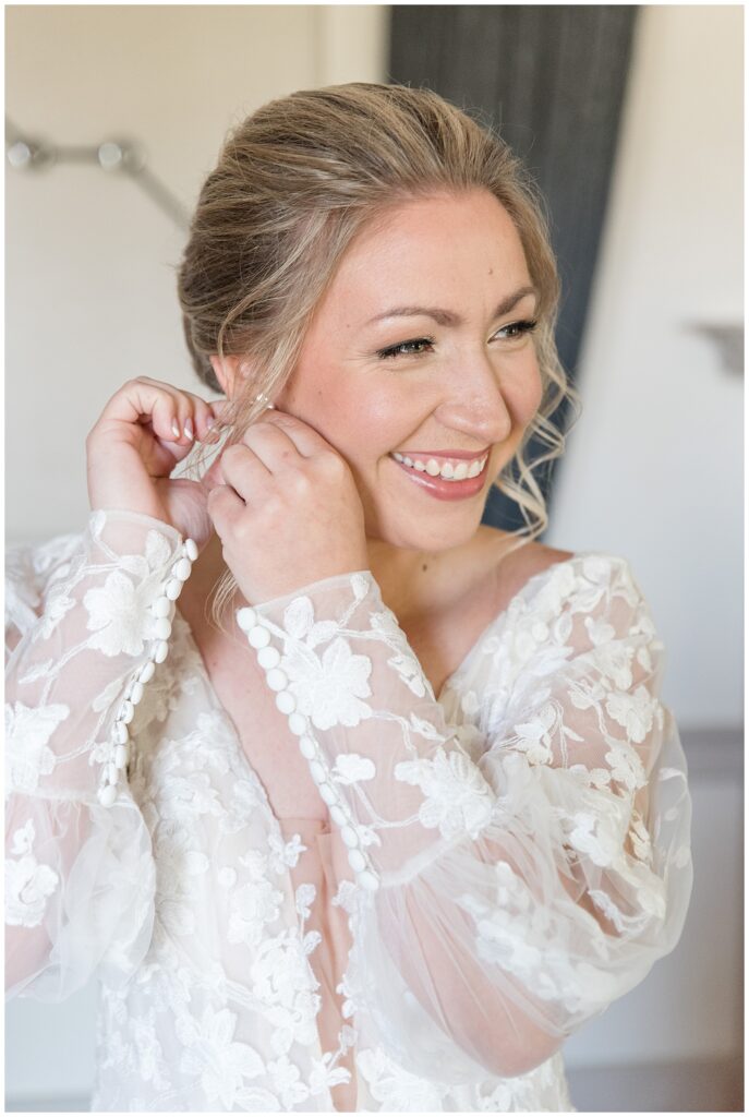 bride smiling as she adjusts her right earring wearing a long-sleeved lacy wedding gown in lancaster county