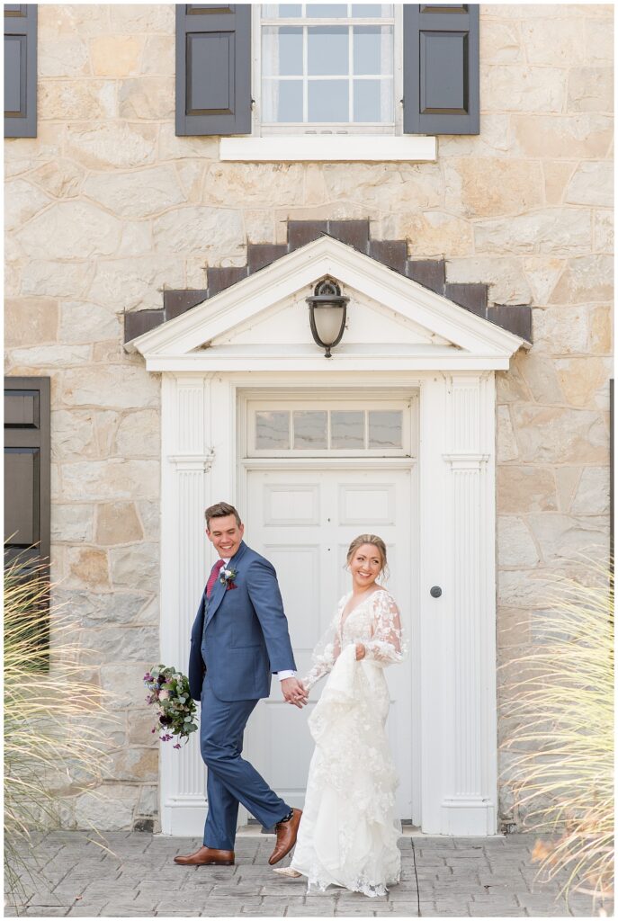 groom leading his bride past white door as they both look back over their left shoulders at the barn at silverstone