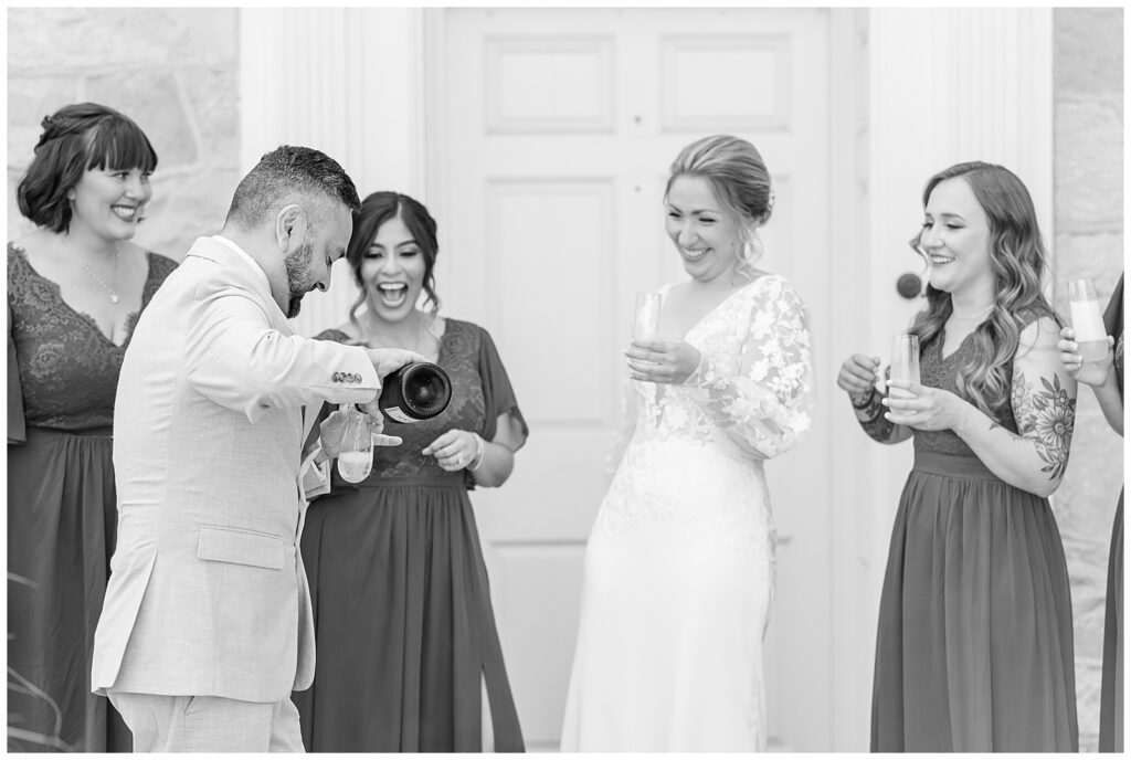 bride with her bridal party laughing as they pour champagne at the barn at silverstone