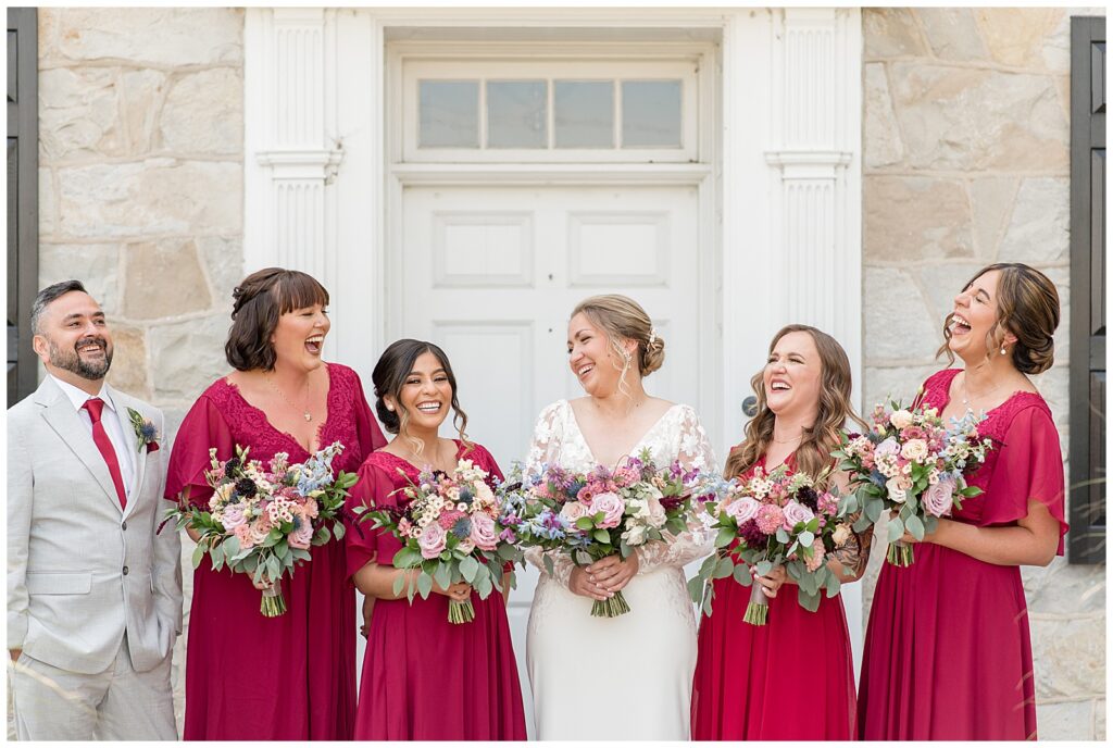 closeup photo of bride with her bridal party as they all slightly lean back laughing by white door in lancaster pa