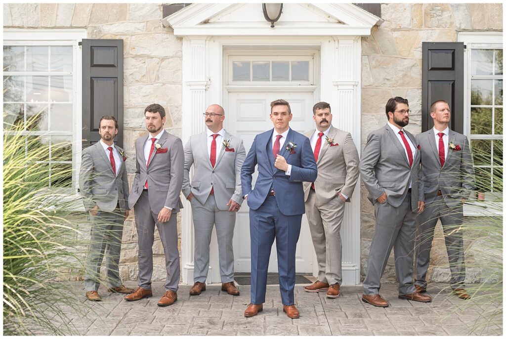 groom looking at the camera as his groomsmen look in different directions by front door of home at the barn at silverstone