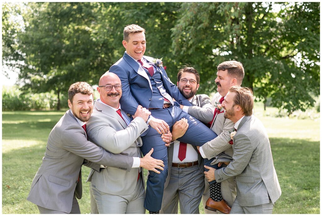 groomsmen lifting groom off the ground as everyone laughs outside at barn wedding in lancaster  county