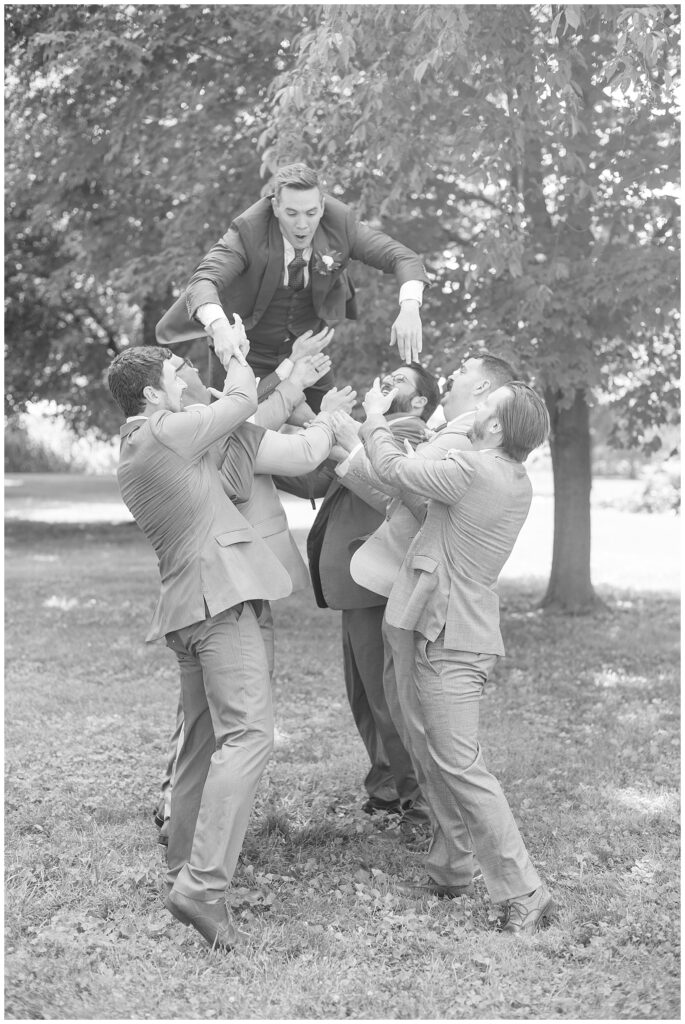 black and white photo of groomsmen lifting groom off the ground outside at the barn at silverstone in lancaster pa