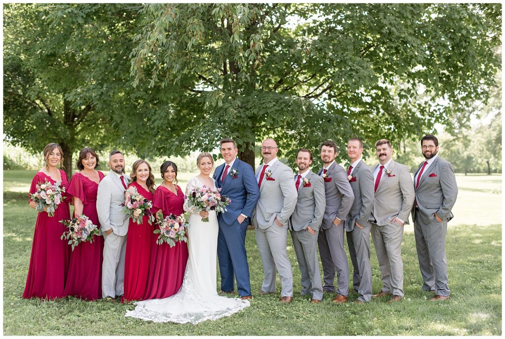 bride and groom surrounded by their bridal party outside with tree in background at the barn at silverstone