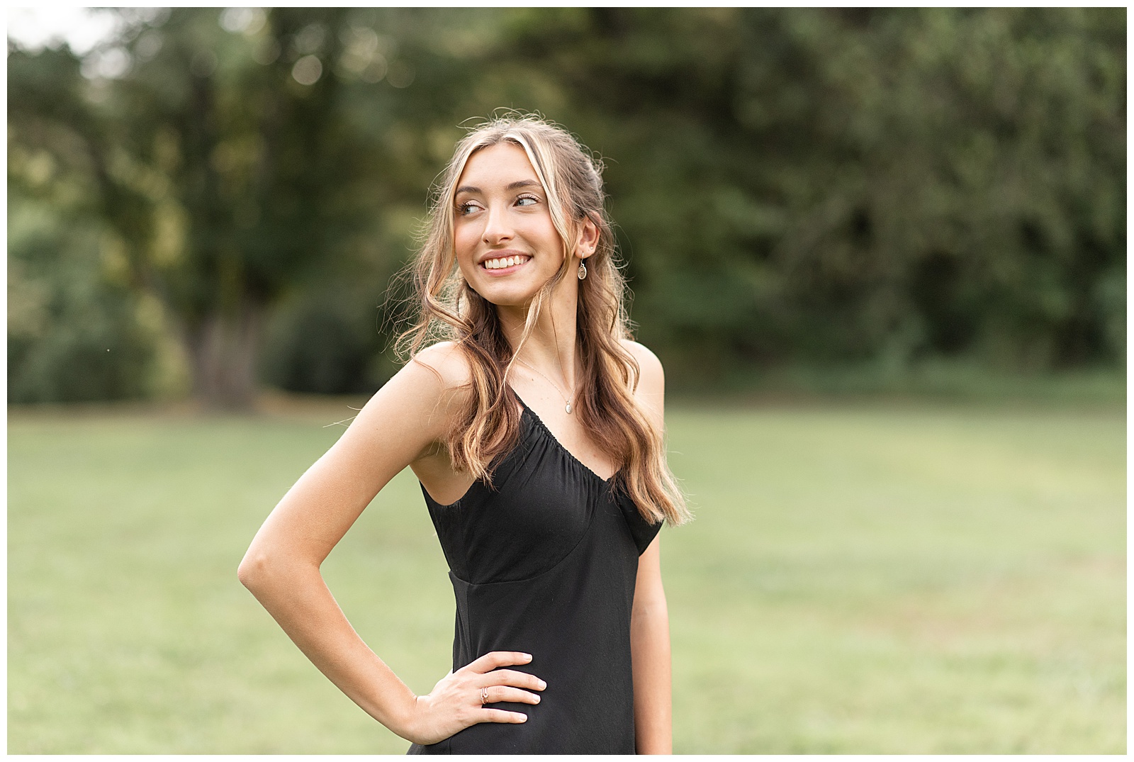 senior girl wearing black dress with right hand on hip and looking back over right shoulder at lancaster county central park