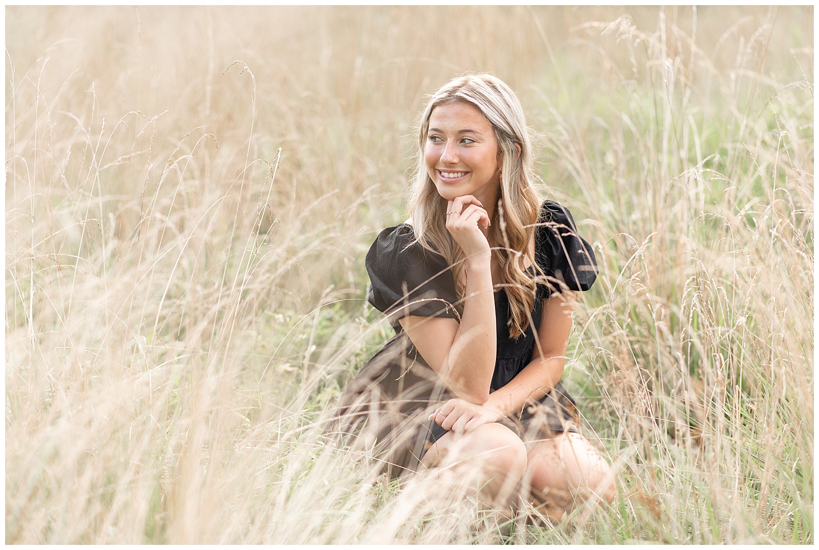 senior girl crouched down in tall dried wild grasses with her chin on her right hand at lancaster county park