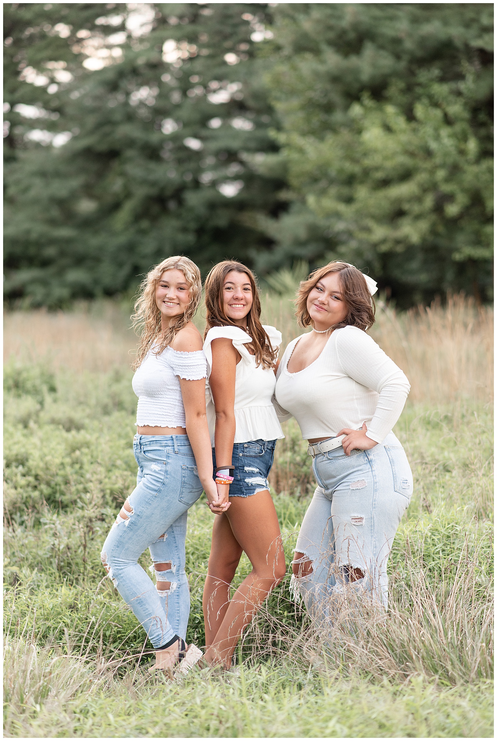 three senior girls all wearing white tops and blue jeans standing together in field of grasses at lancaster county park