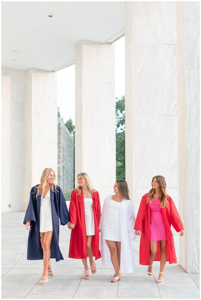 four girls walking towards camera with their graduation gowns open and their white and pink dresses underneath by white columns in hershey pa