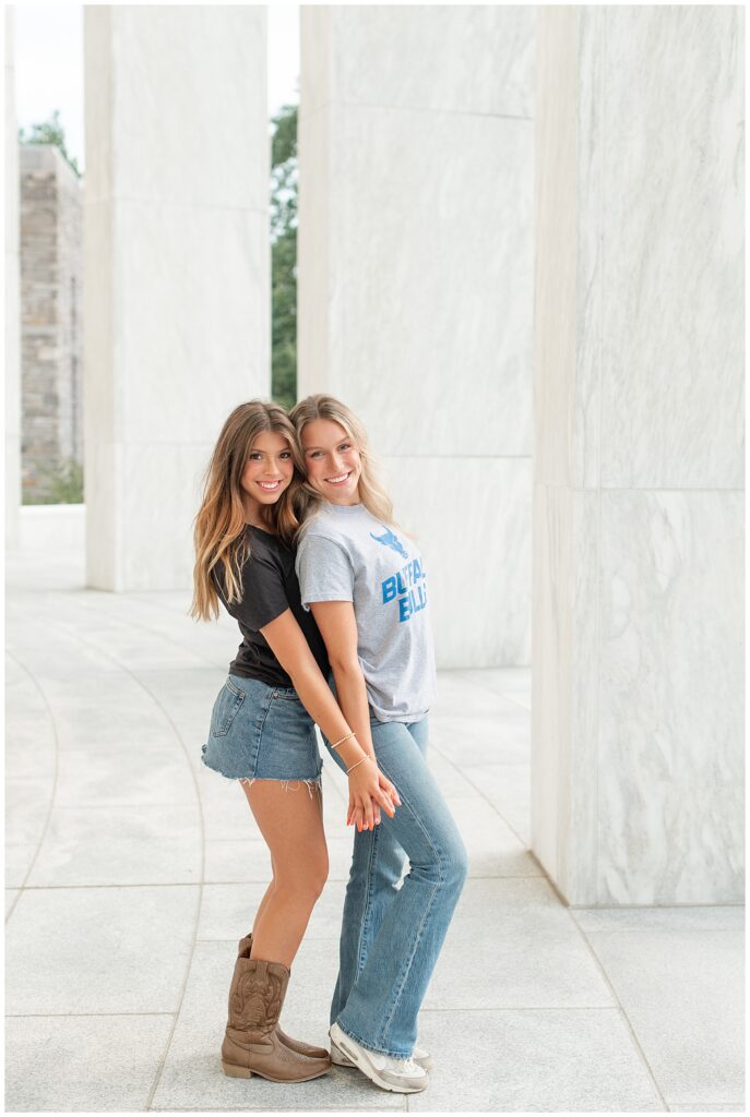two senior girls hugging tightly with hands held by large white columns at founders hall 