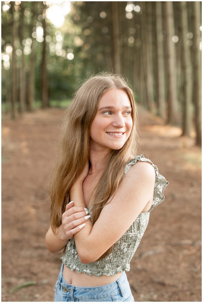 senior girl wearing green floral tank looking over left shoulder and smiling by trees at overlook park