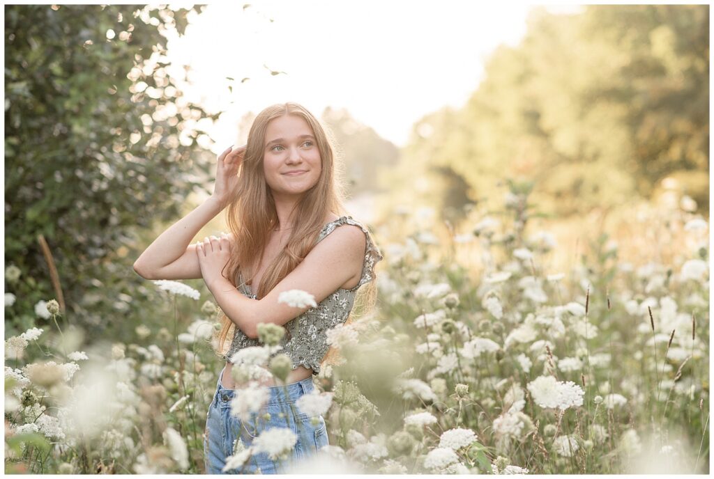 senior girl standing in field of queen anne's lace flowers with her right hand in her hair at sunset at overlook park