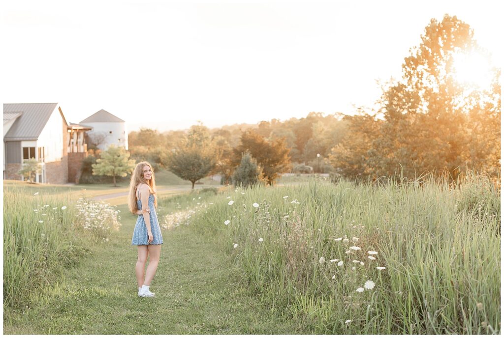 senior girl walking away from camera looking back over right shoulder by field of wildflowers at overlook park in manheim township