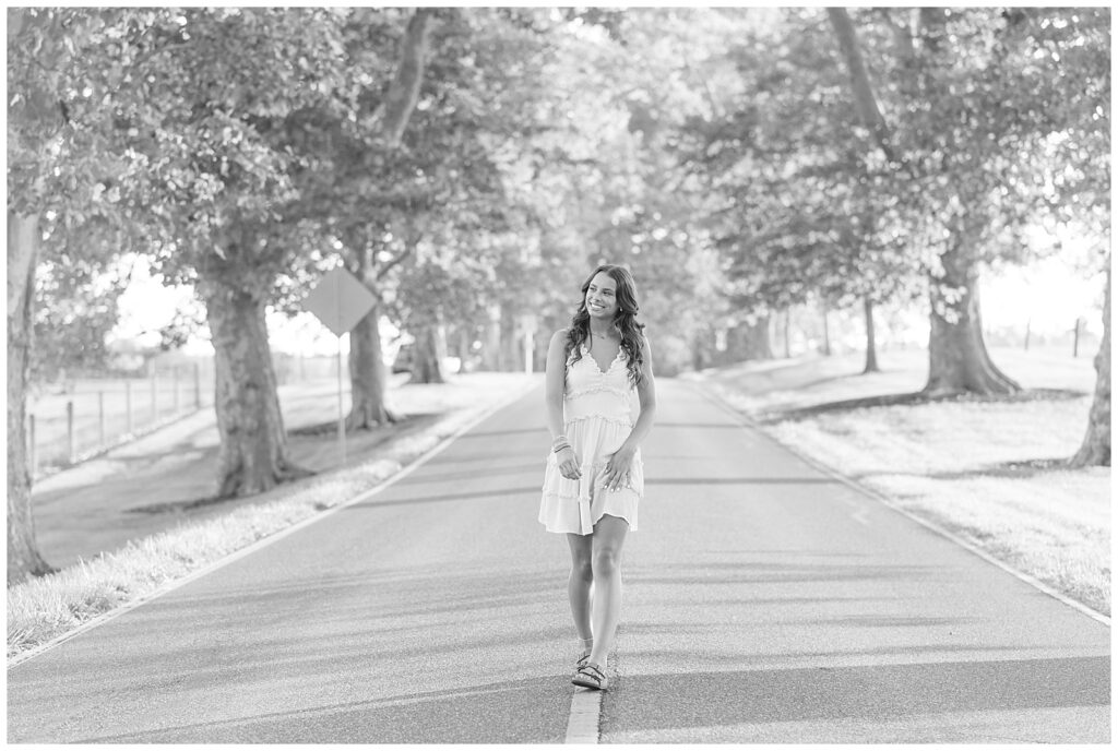 black and white photo of senior girl walking on line in middle of road wearing white dress at masonic village