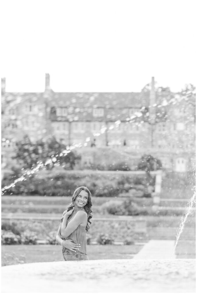 black and white photo of senior girl looking back over left shoulder with water fountain spraying in front of her at masonic village
