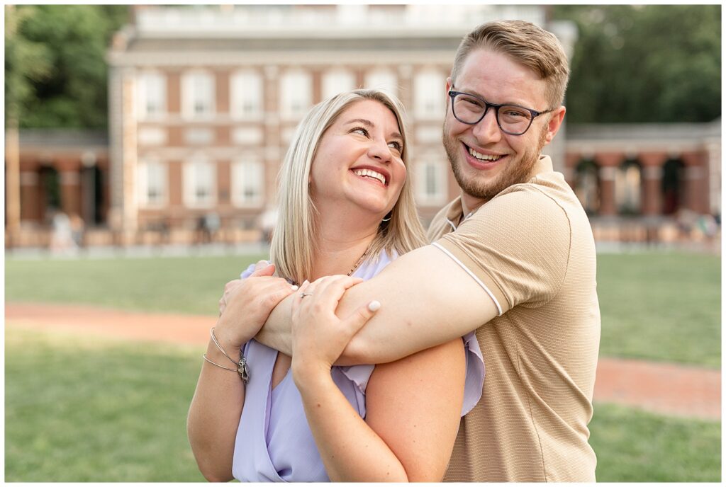 guy hugging girl from behind as she looks back smiling at him near independence hall in pennsylvania