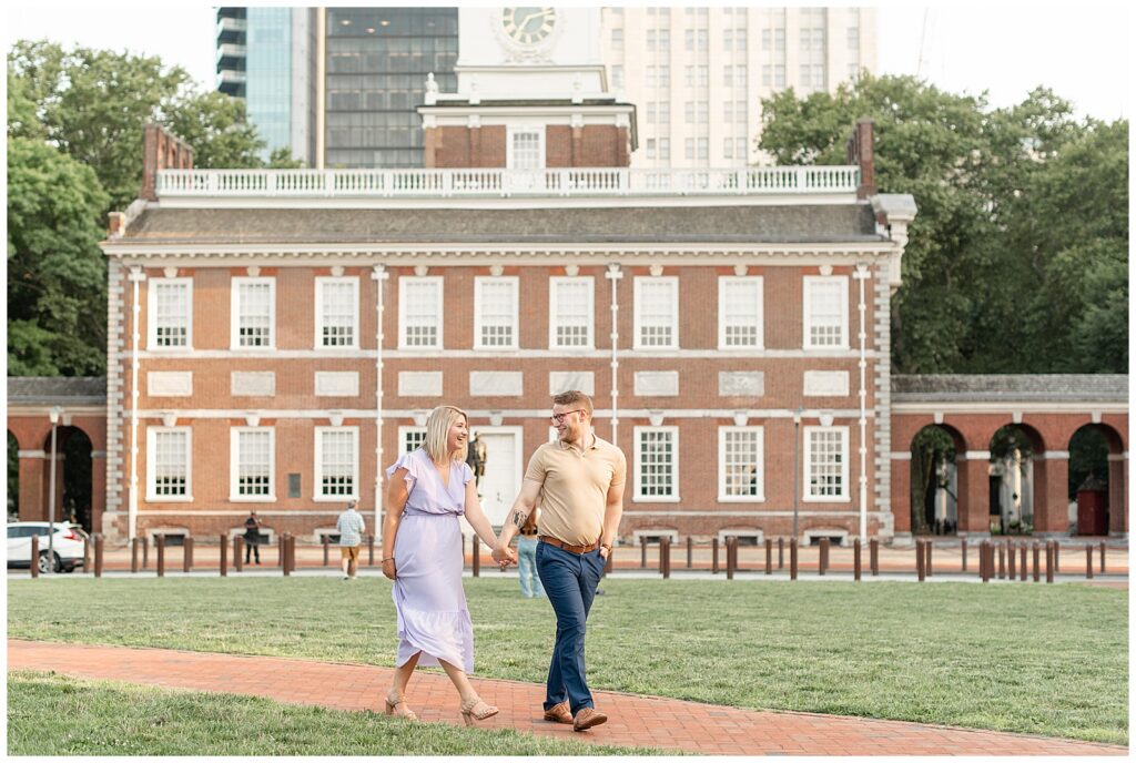 couple holding hands and walking along path near independence hall in philadelphia