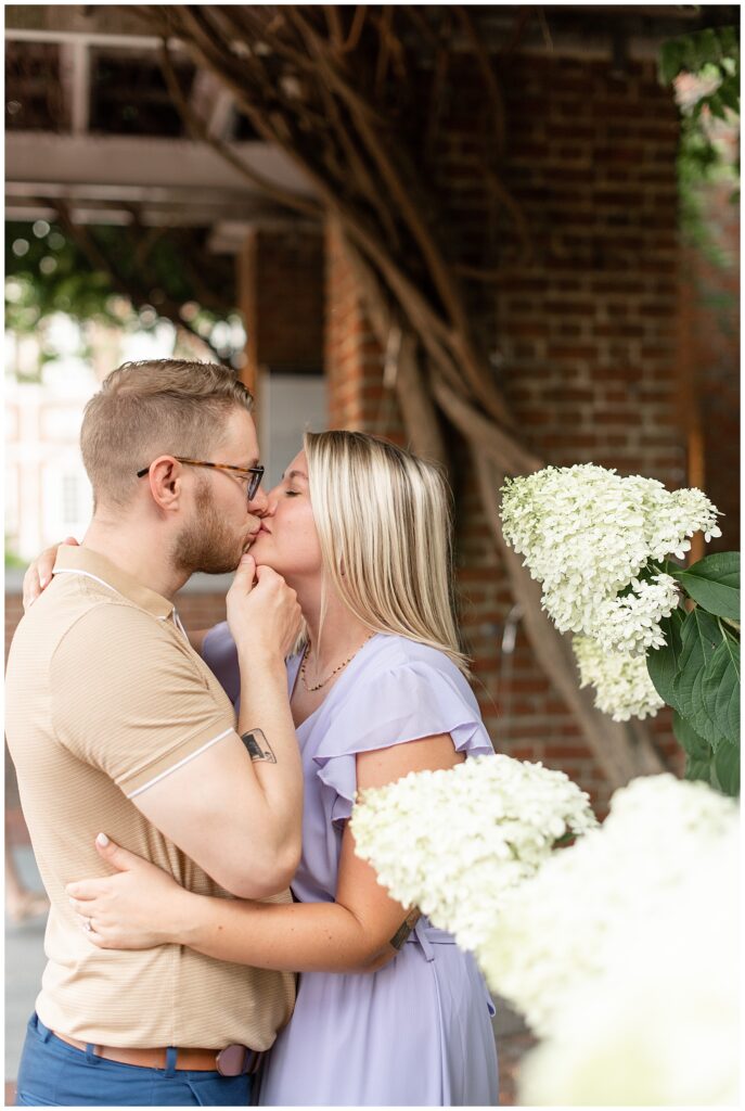 guy holding girl's chin as they kiss by white hydrangea bush in philadelphia pennsylvania