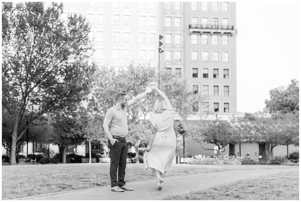 black and white photo of woman twirling under guy's left hand by tall building in philadelphia pennsylvania