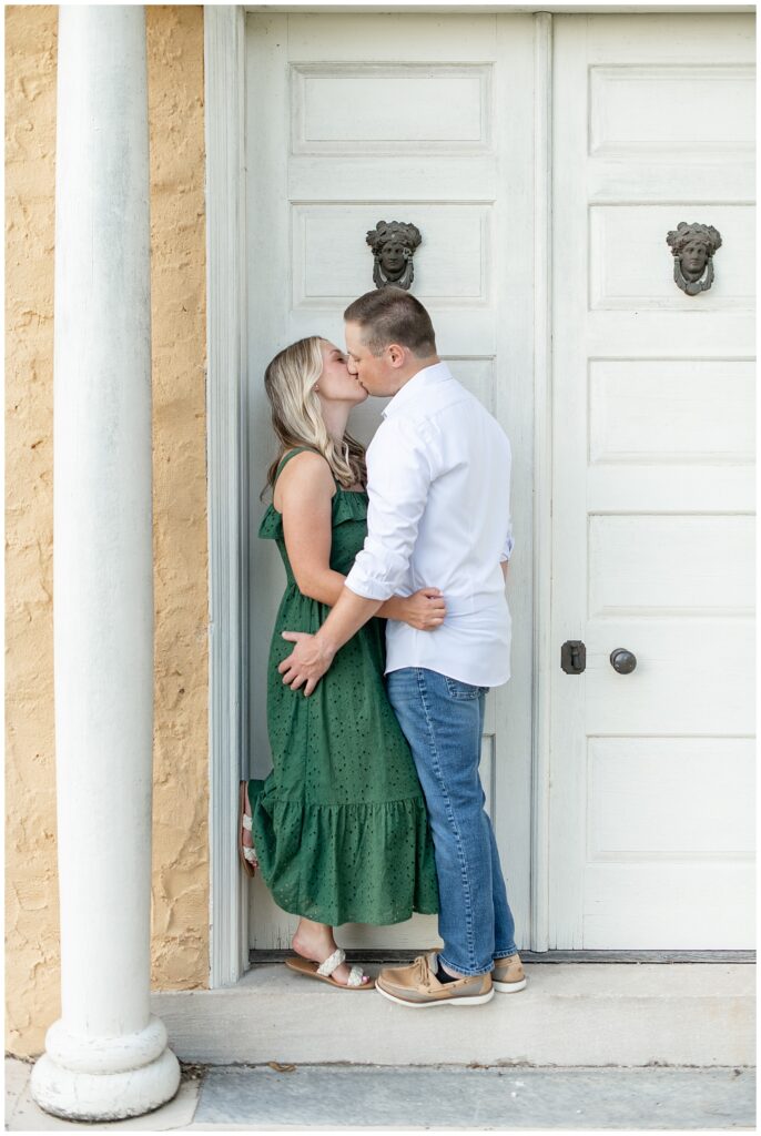 engaged couple kissing by white door of peach colored house at hibernia park