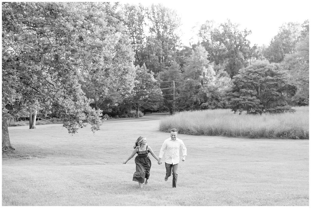 black and white photo of couple holding hands and walking in the distance towards the camera at park in chester county