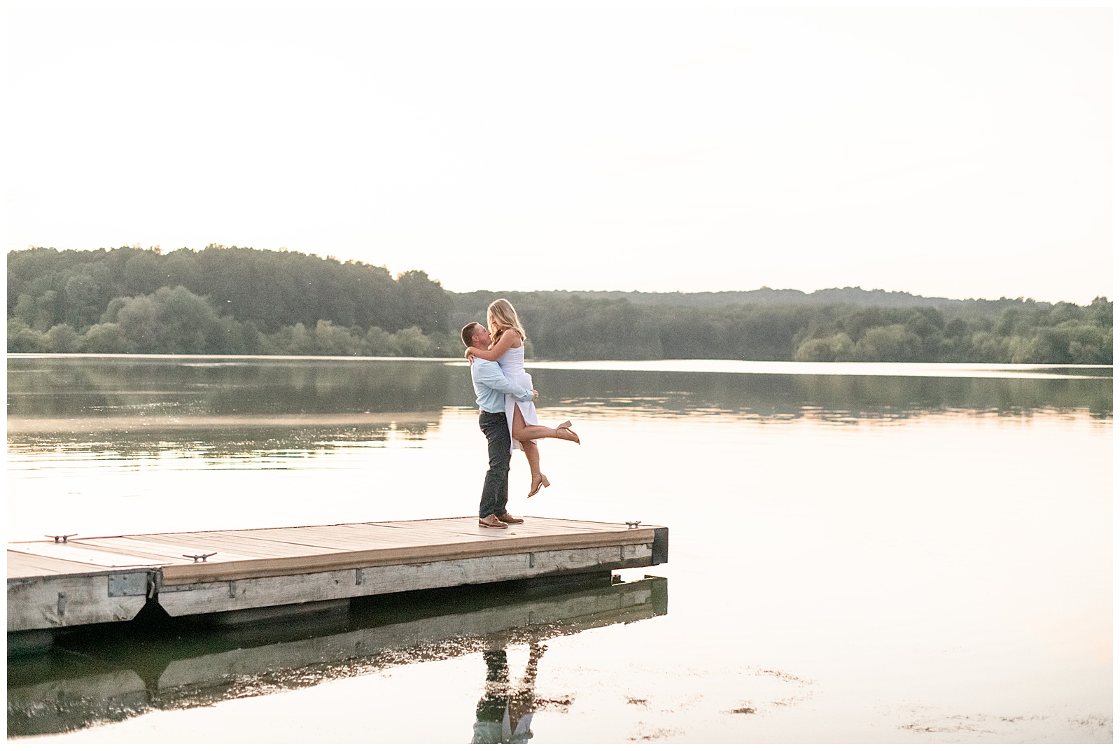 guy lifting girl up off the ground at the end of long wooden dock by lake at sunset at hibernia park in pennsylvania