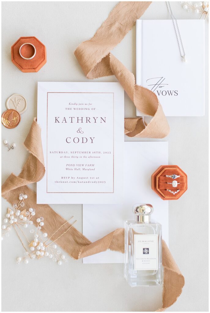 wedding invitation and rings in orange velvet boxes and other wedding details on display in white hall maryland