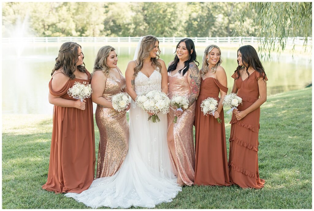 bride with her five bridesmaids all wearing rust and copper color dresses in different colors and styles by pond in harford maryland