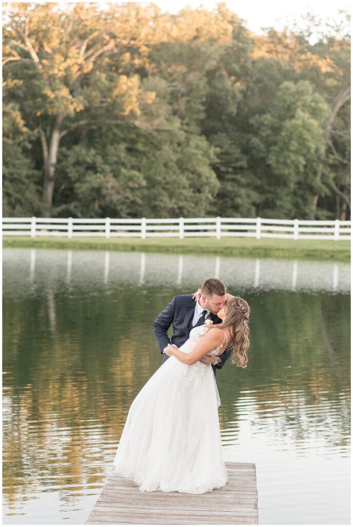 couple kissing by pond as groom slightly dips back his bride at pond view farm