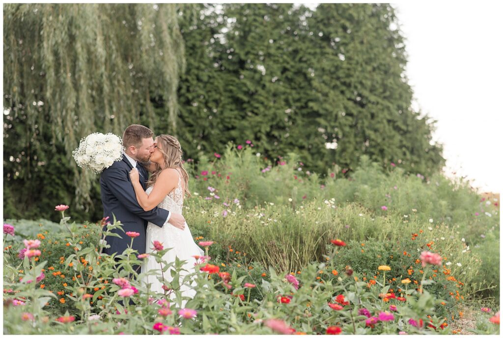 couple standing on left side of photo in field of wildflowers kissing at pond view farm