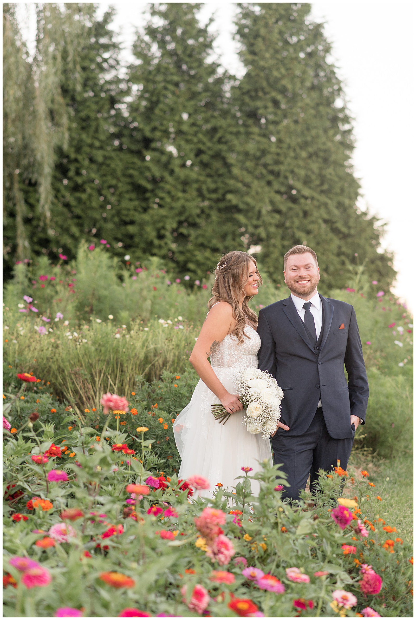 bride looking at her groom as he smiles at the camera in wildflower field at pond view farm in maryland